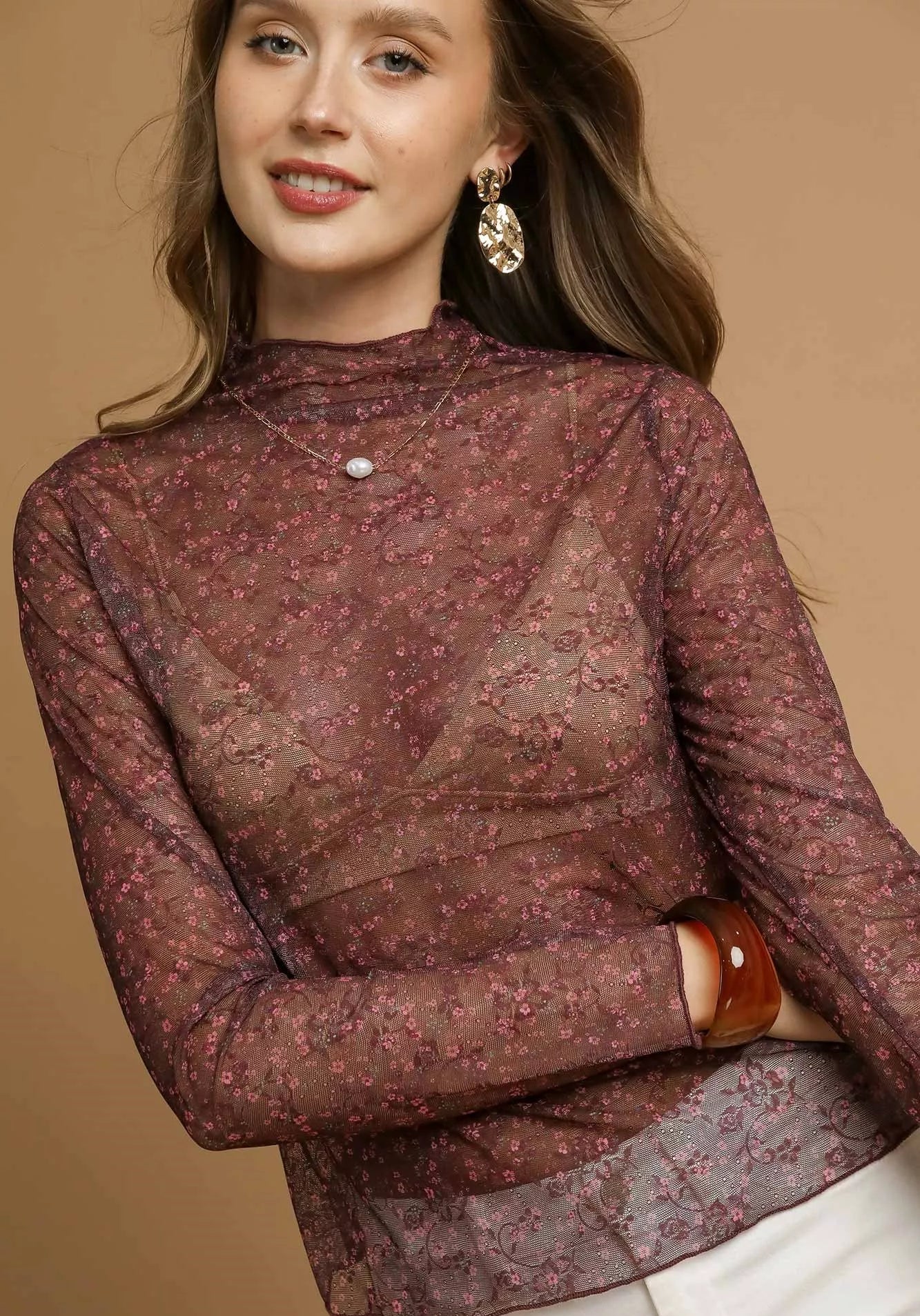 Woman wearing a burgundy floral blouse against a beige background