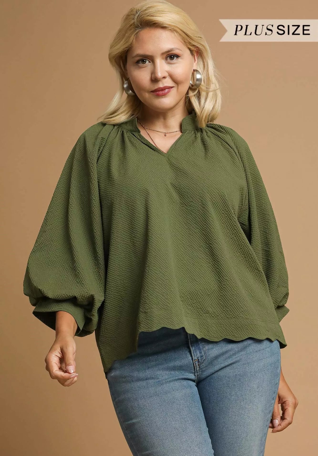 Woman wearing an olive green blouse and blue jeans on a beige background