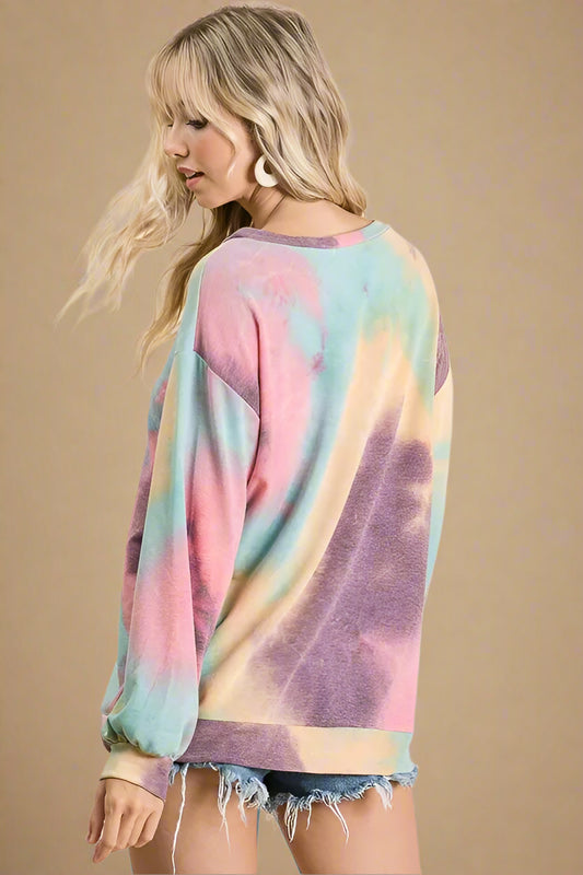 Woman wearing a colorful tie-dye long-sleeve shirt against a beige background