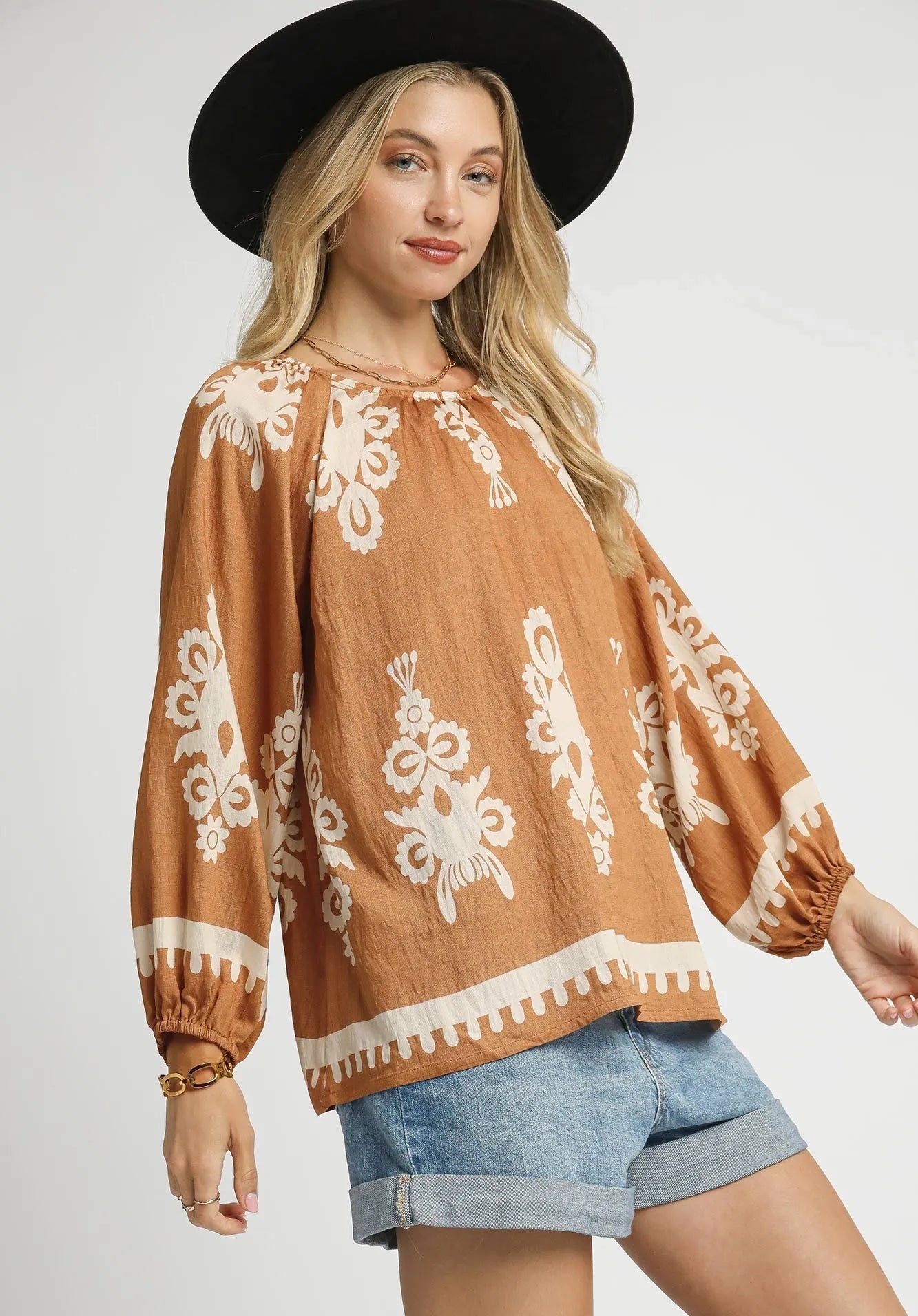 Woman wearing a brown blouse with white embroidery and denim shorts on a white background