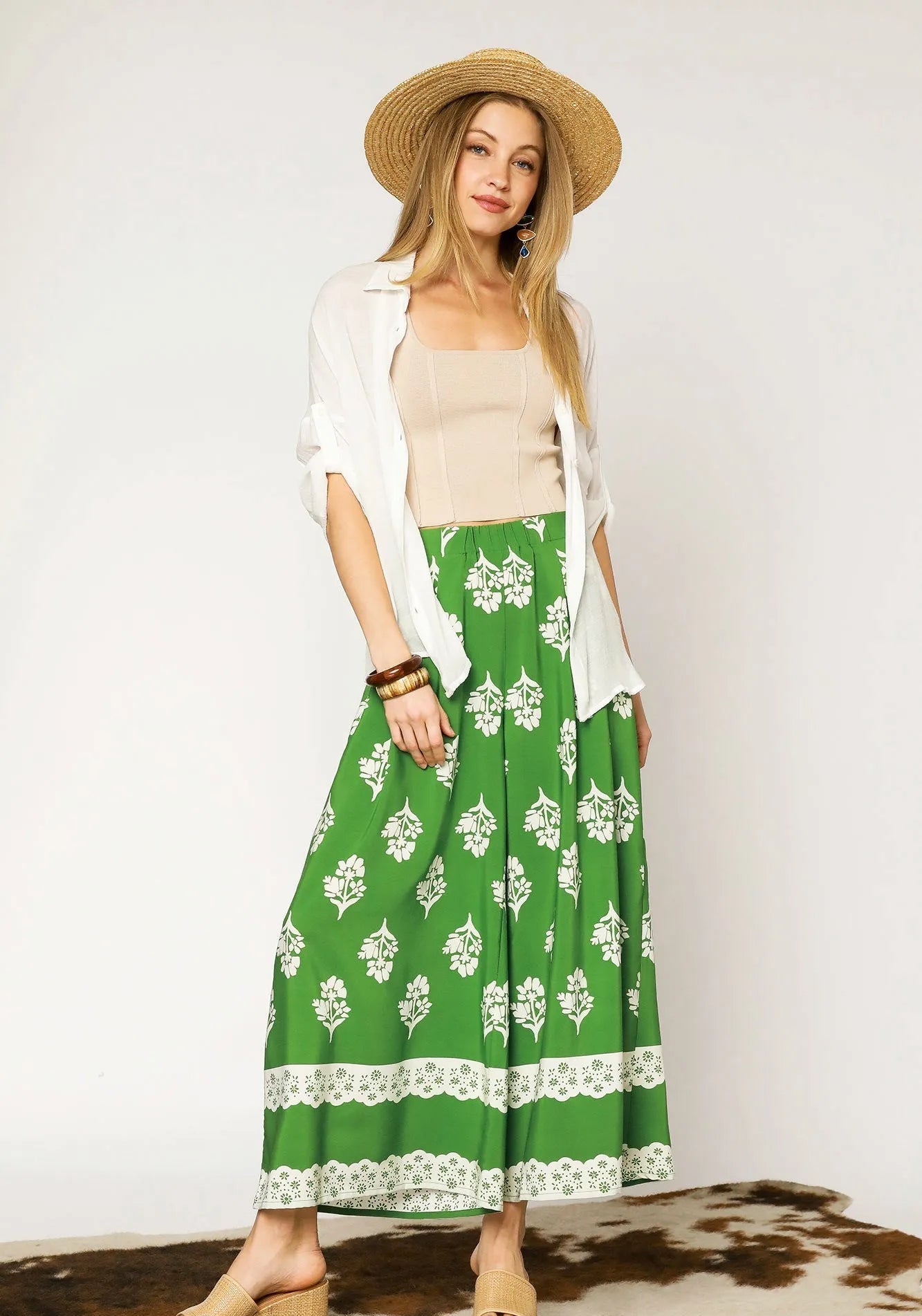 Woman wearing a green patterned skirt with a white top and straw hat on a plain background