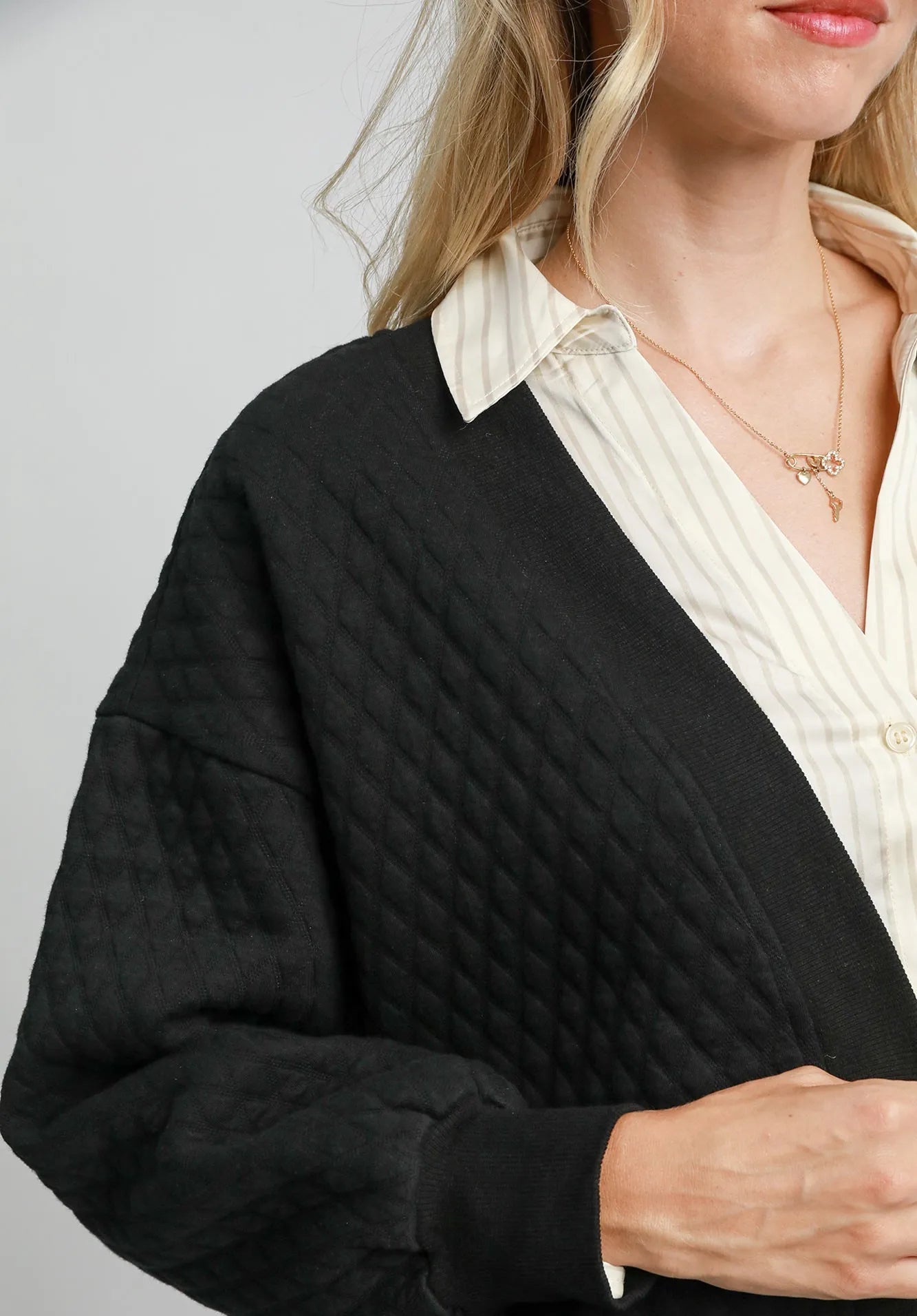 Person wearing a black quilted jacket over a white shirt with a neutral background