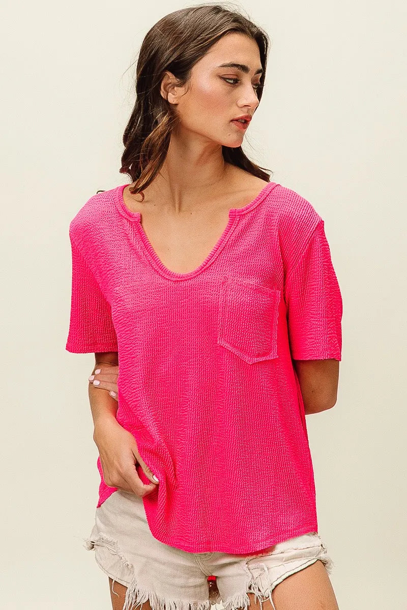 Woman wearing a bright pink textured top with a pocket on a beige background