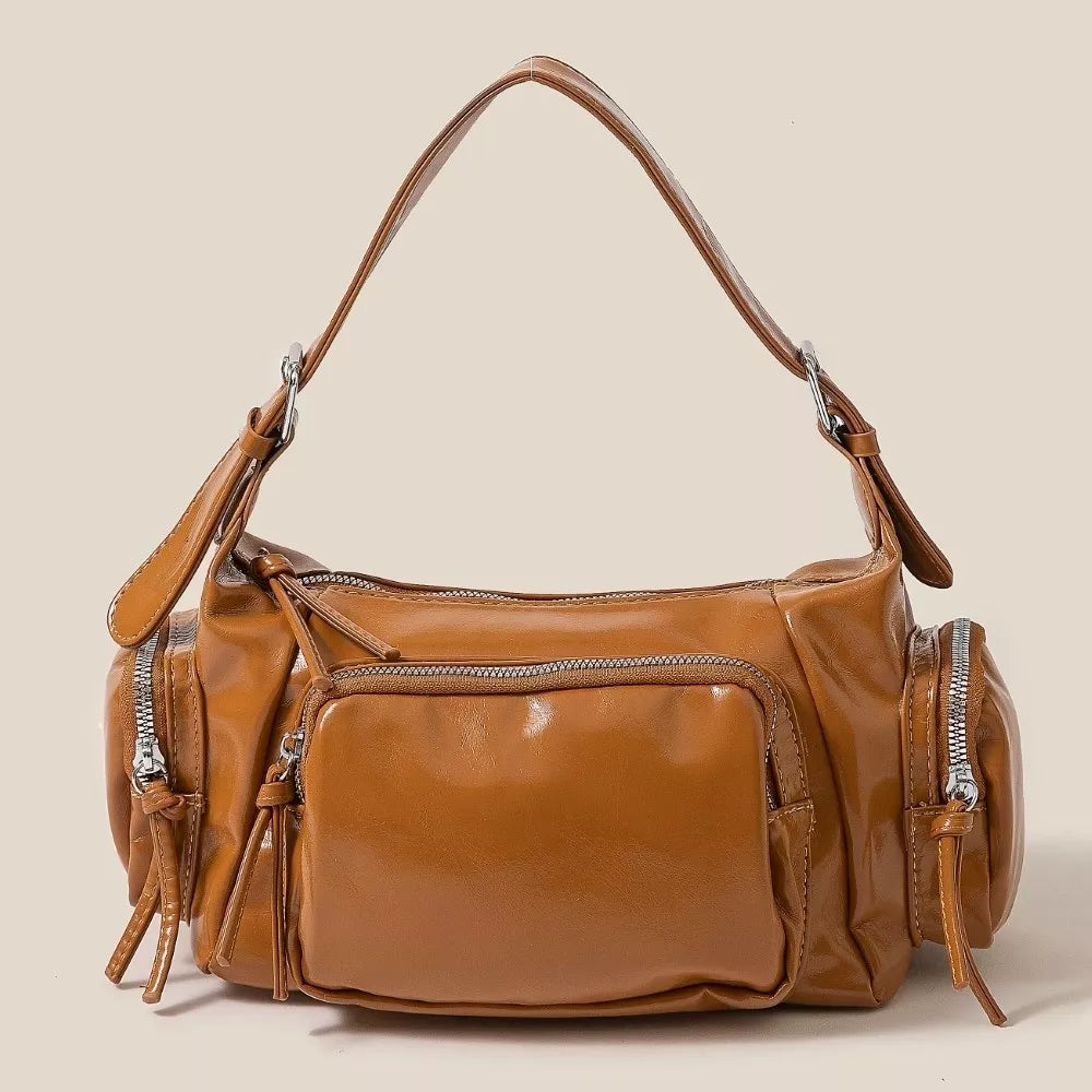 Brown leather handbag with multiple zippers on a beige background