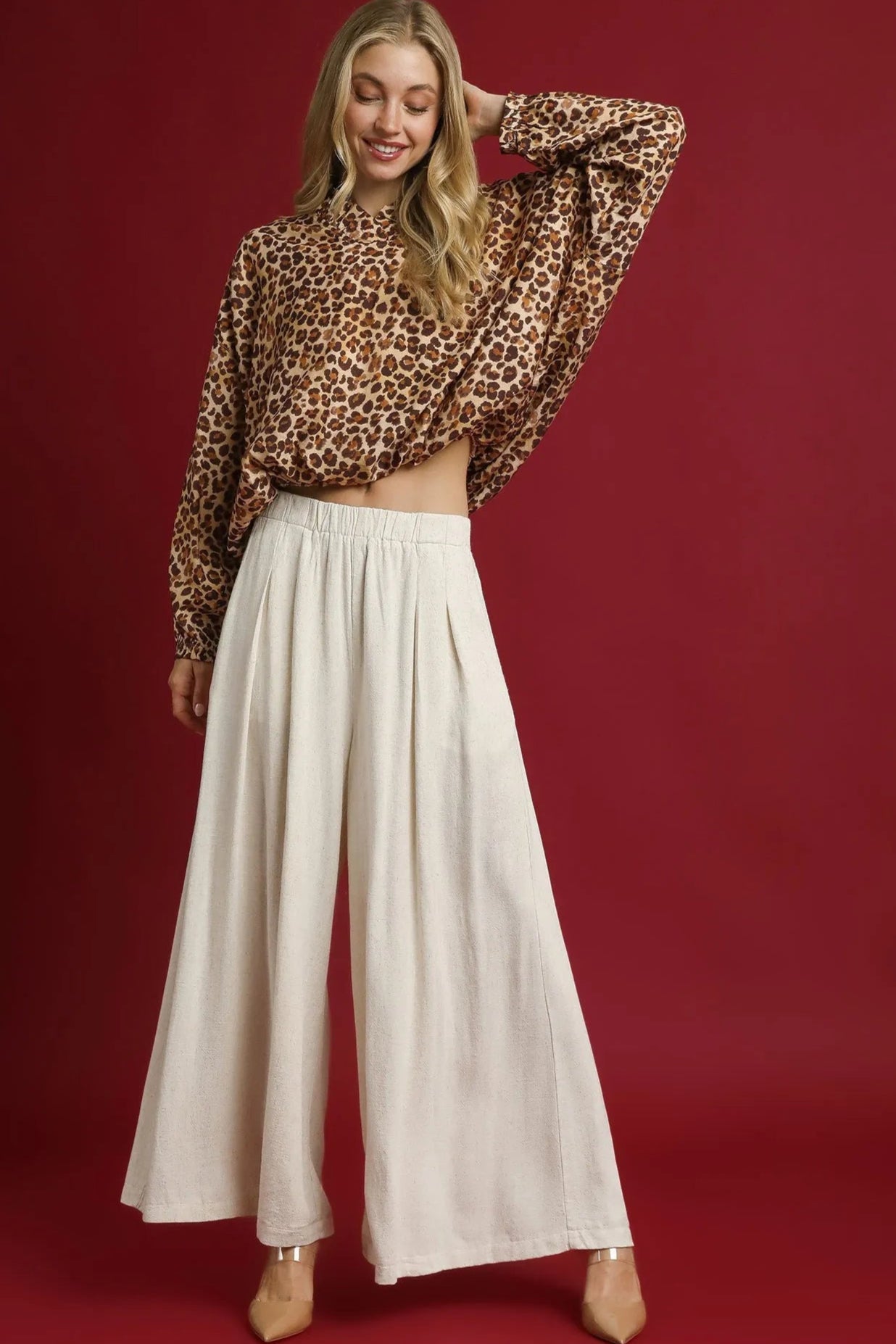 Woman wearing a leopard print top and white pants on a red background