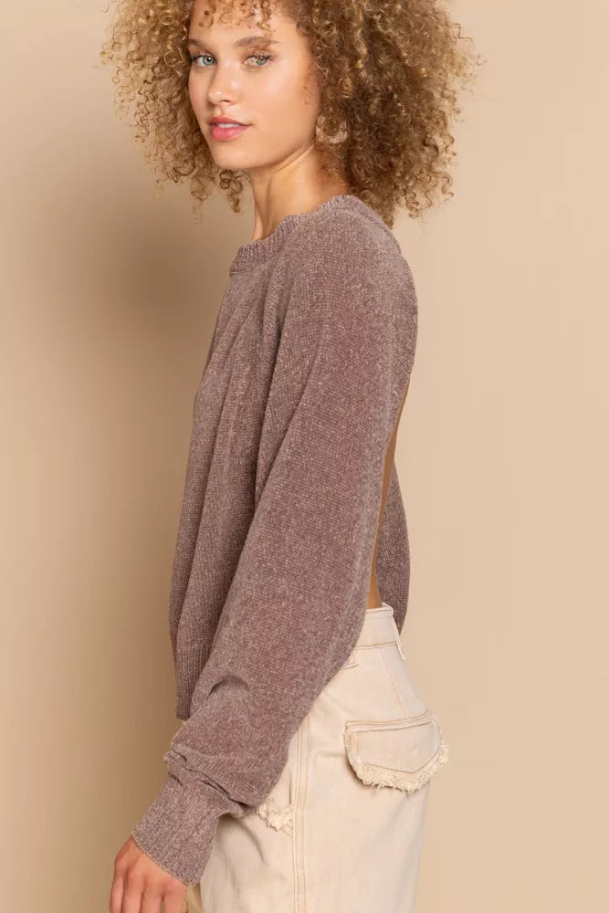 Woman wearing a brown sweater and beige pants against a beige background