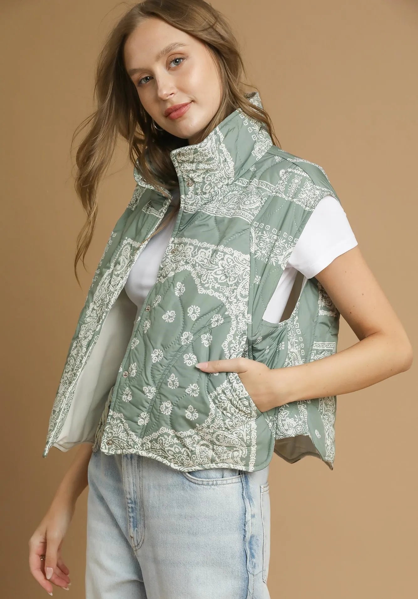 Woman wearing a green patterned vest over a white shirt on a beige background