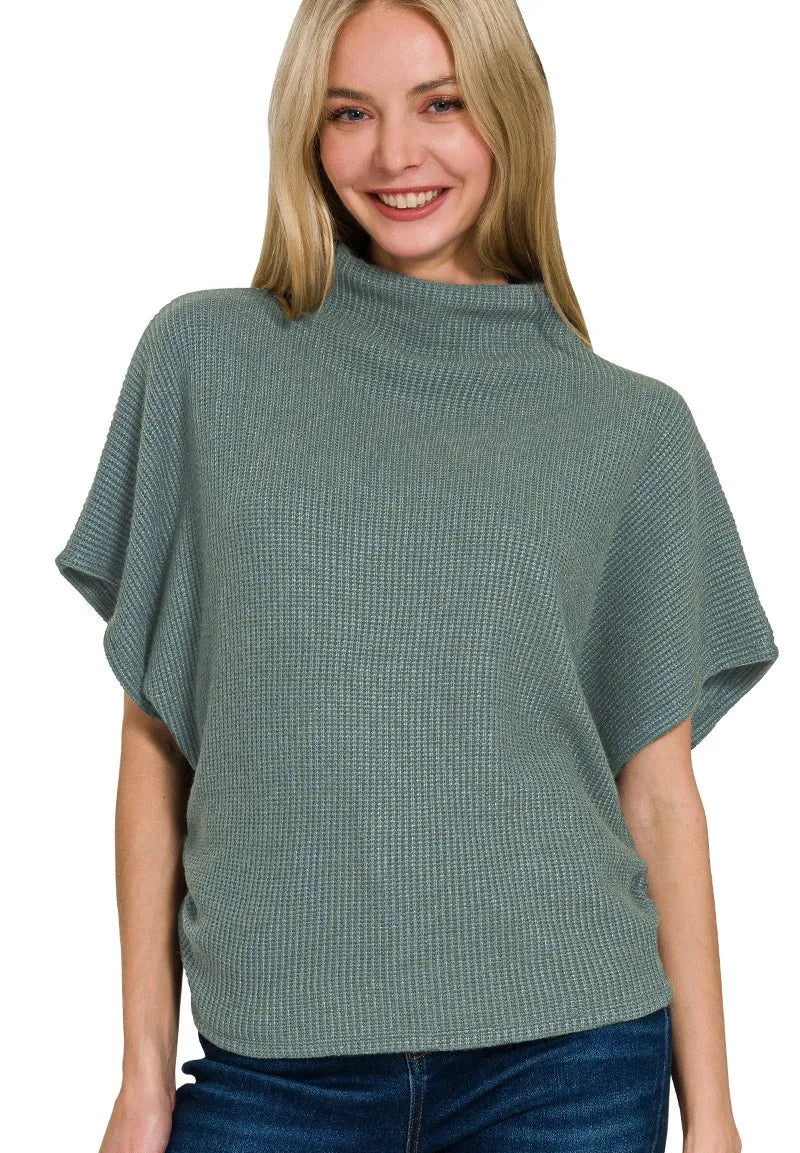 Woman wearing a green poncho over a blue top on a white background