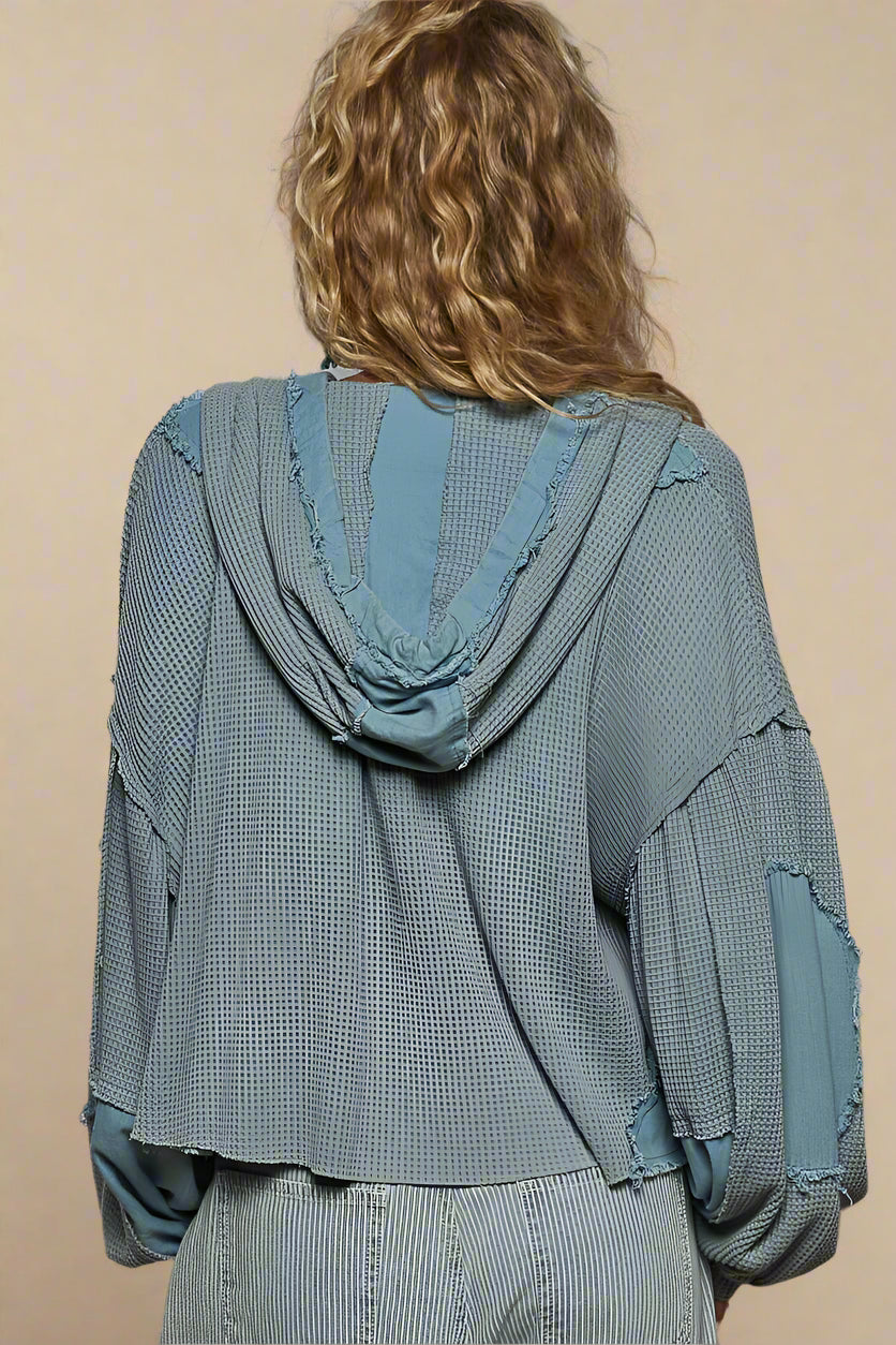 Person wearing a textured green jacket with blue accents on a beige background