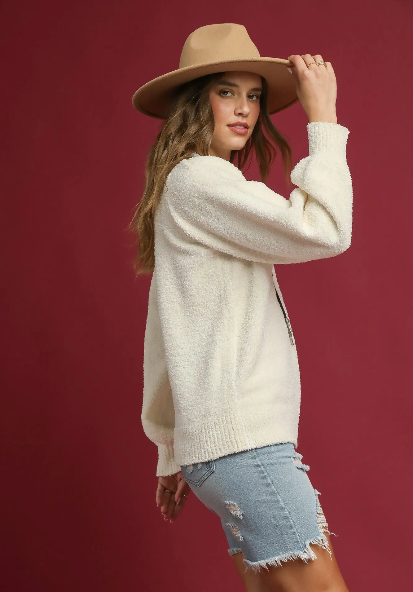 Woman wearing a beige sweater and hat against a red background