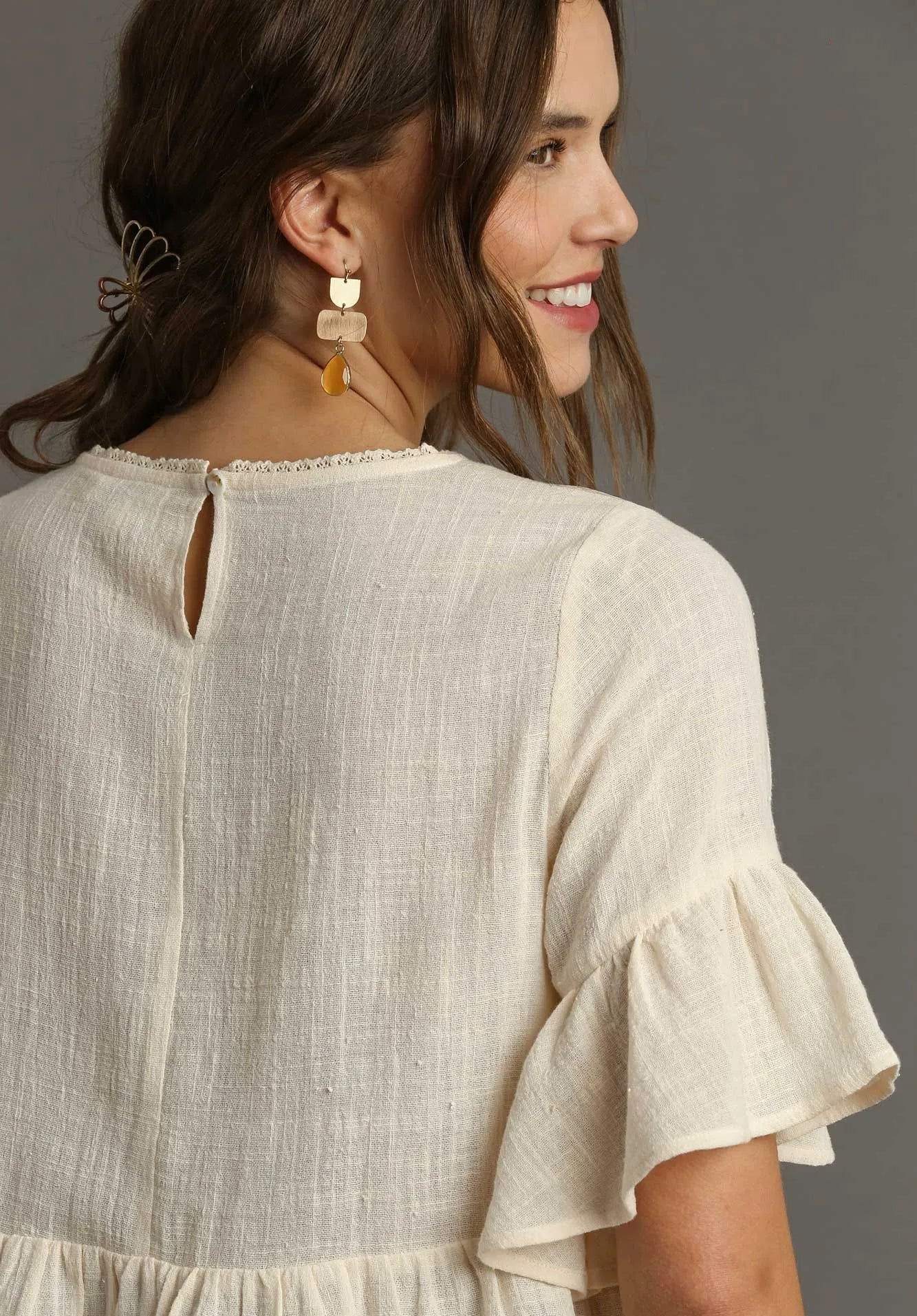 Woman wearing a cream dress with ruffled sleeves against a gray background