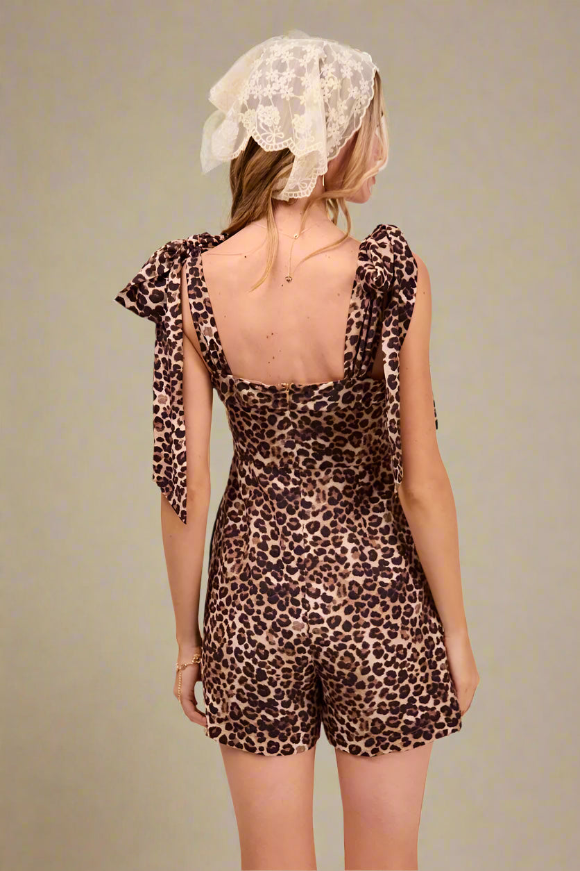 Woman wearing a leopard print romper with a beige headscarf on a plain background