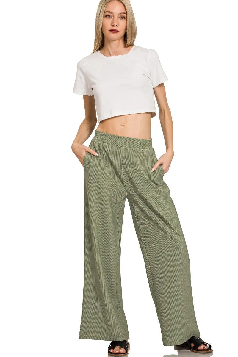 Woman wearing a white crop top and green wide-leg pants on a white background