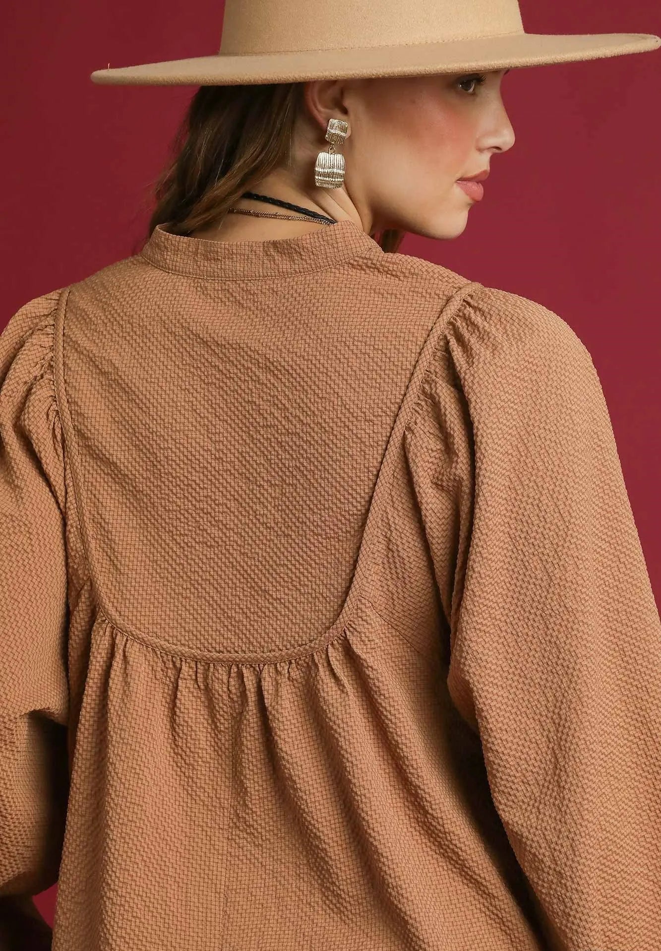 Woman wearing a brown textured dress and beige hat against a red background