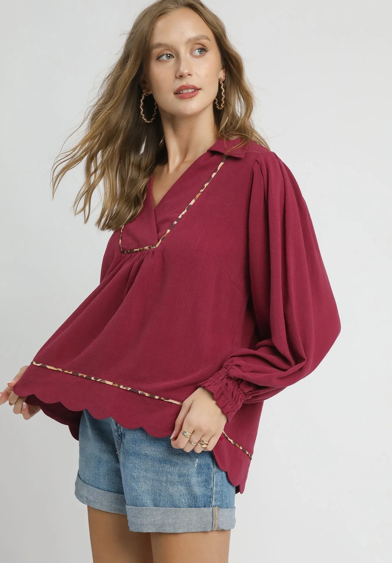 Woman wearing a burgundy blouse with gold trim on a plain background