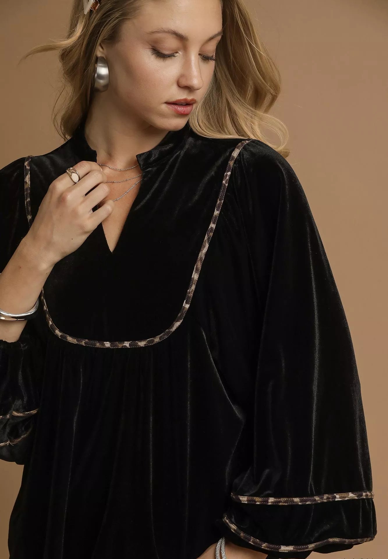 Woman wearing a black velvet dress with leopard print trim on a brown background