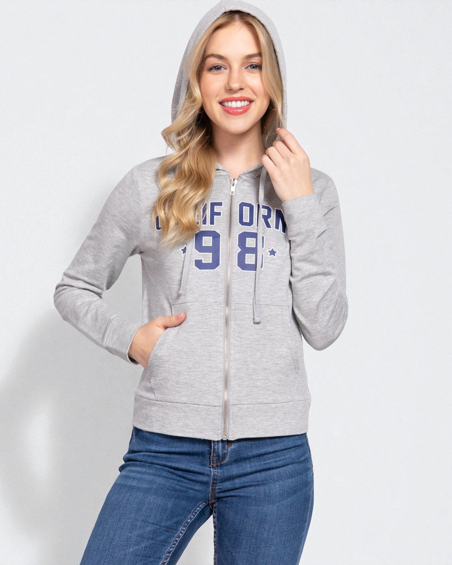 Woman wearing a gray hoodie with text and blue jeans on a light gray background