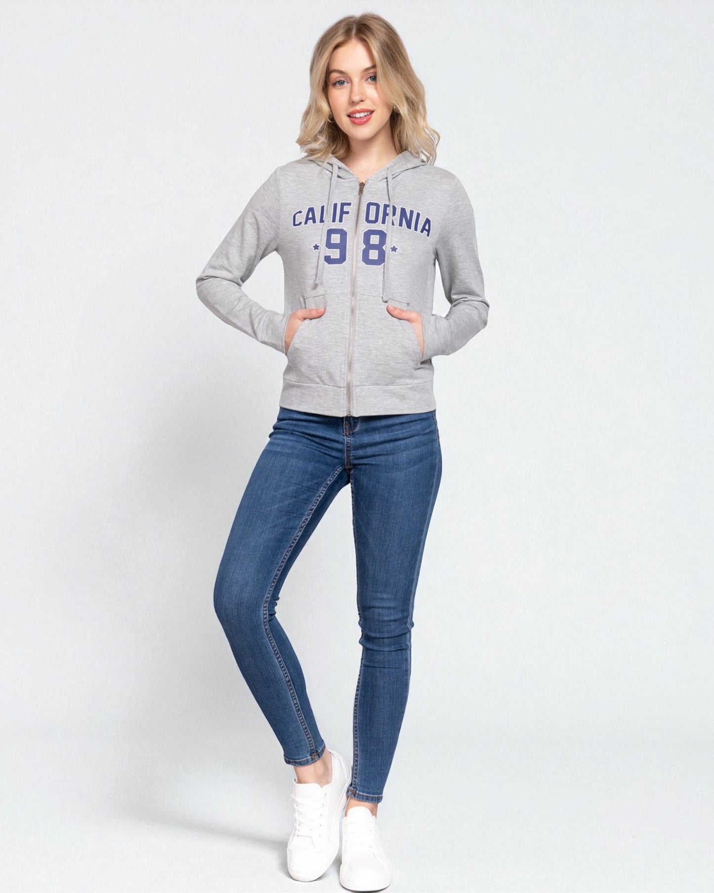 Woman wearing a gray hoodie with 'California 98' text and blue jeans on a white background