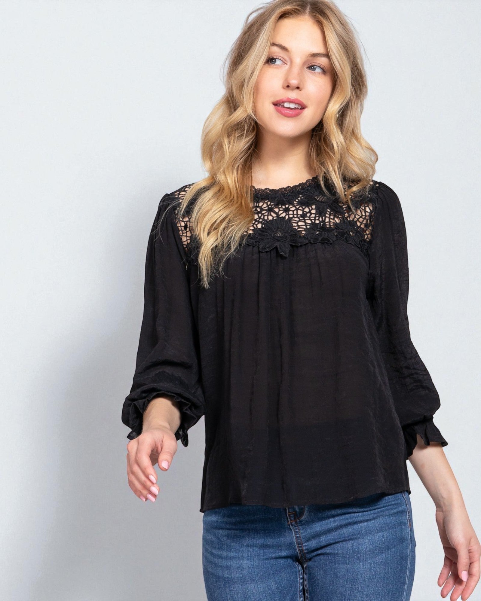 Woman wearing a black blouse with lace details on a light gray background