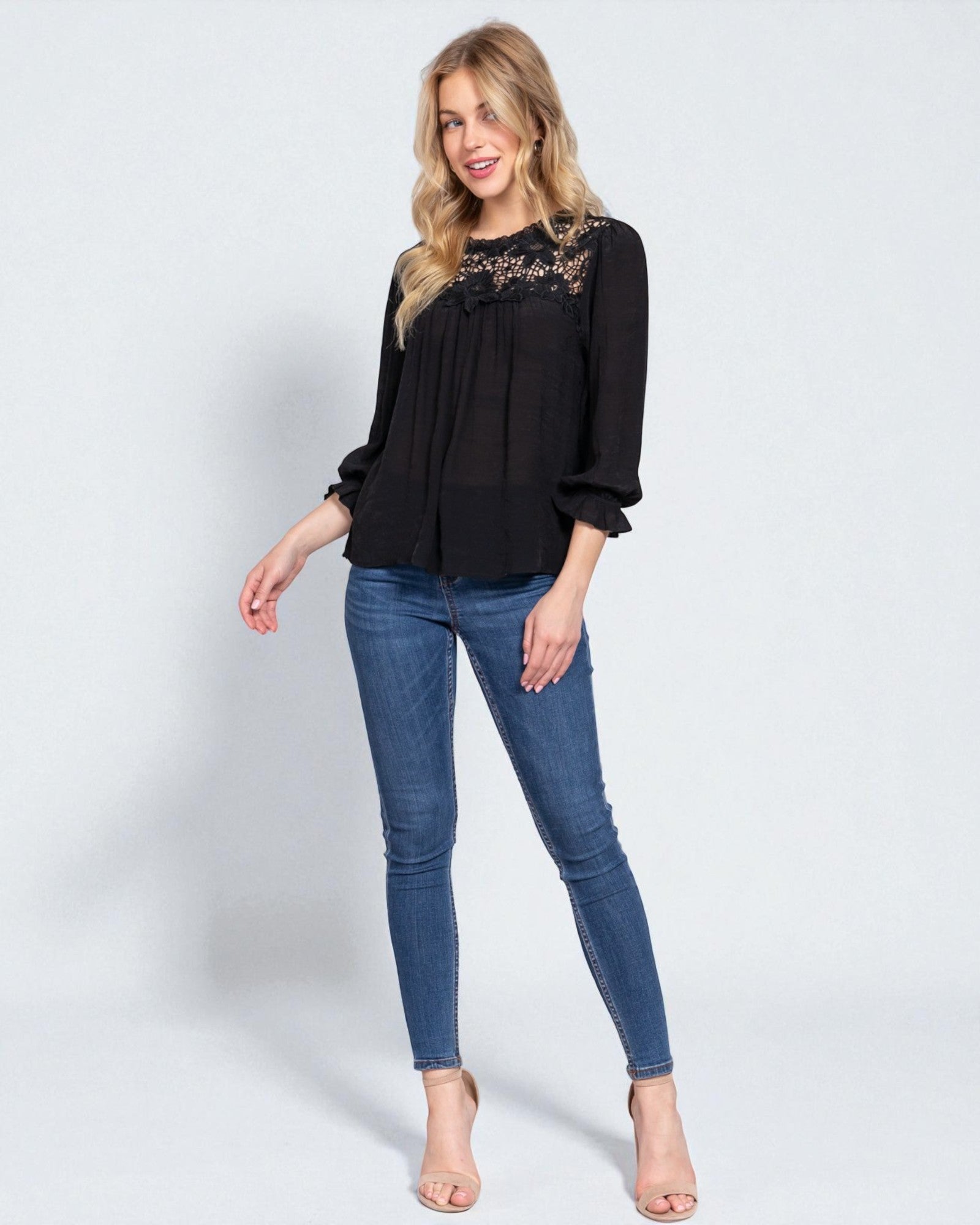 Woman wearing a black blouse with lace details and blue jeans on a white background