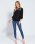 Woman wearing a black blouse with lace details and blue jeans on a white background