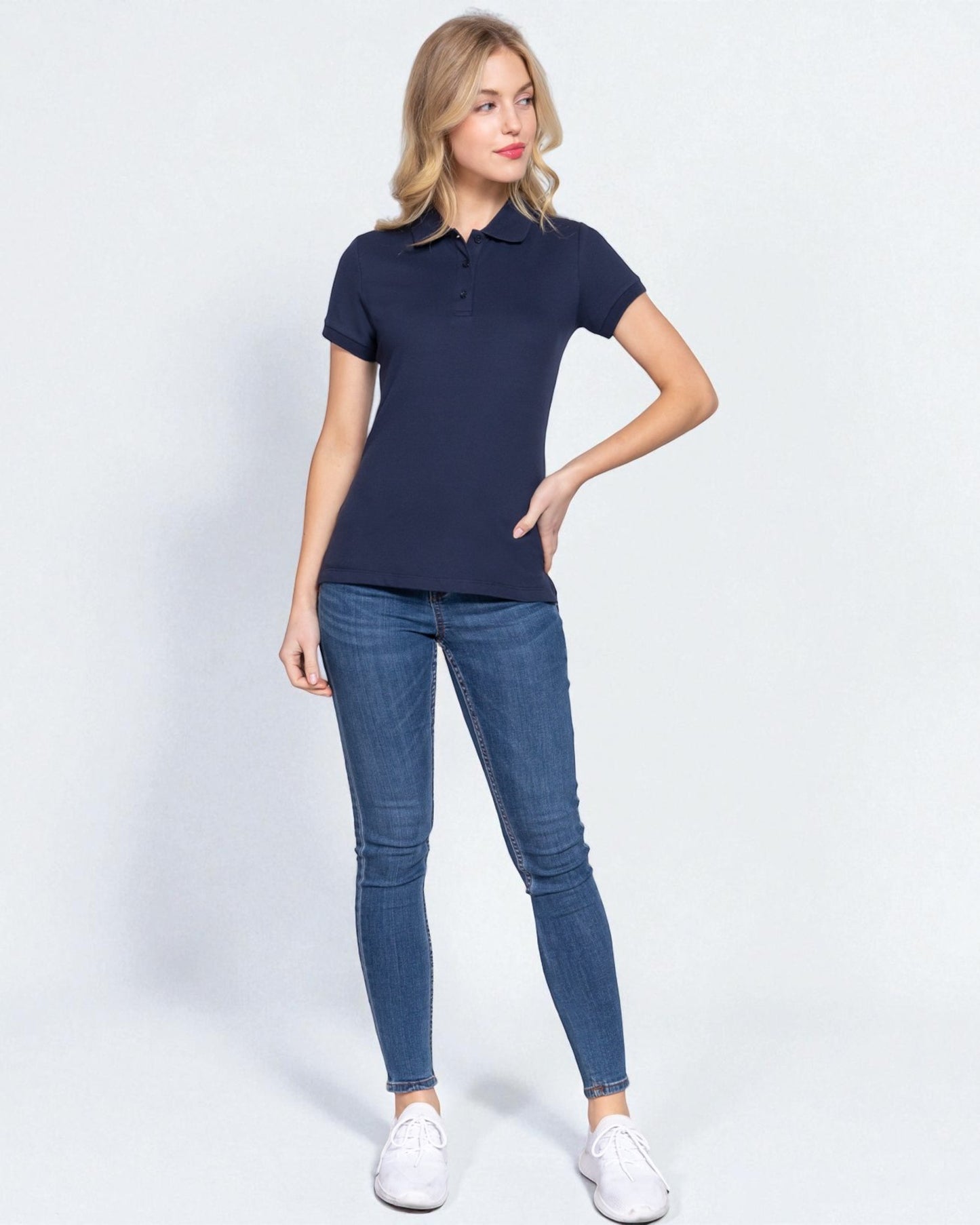 Woman wearing a navy polo shirt and blue jeans on a white background