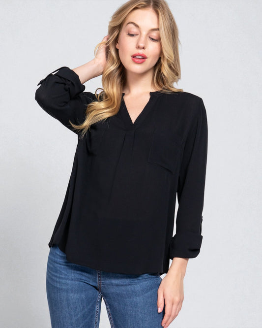 Woman wearing a black blouse with long sleeves and blue jeans on a gray background