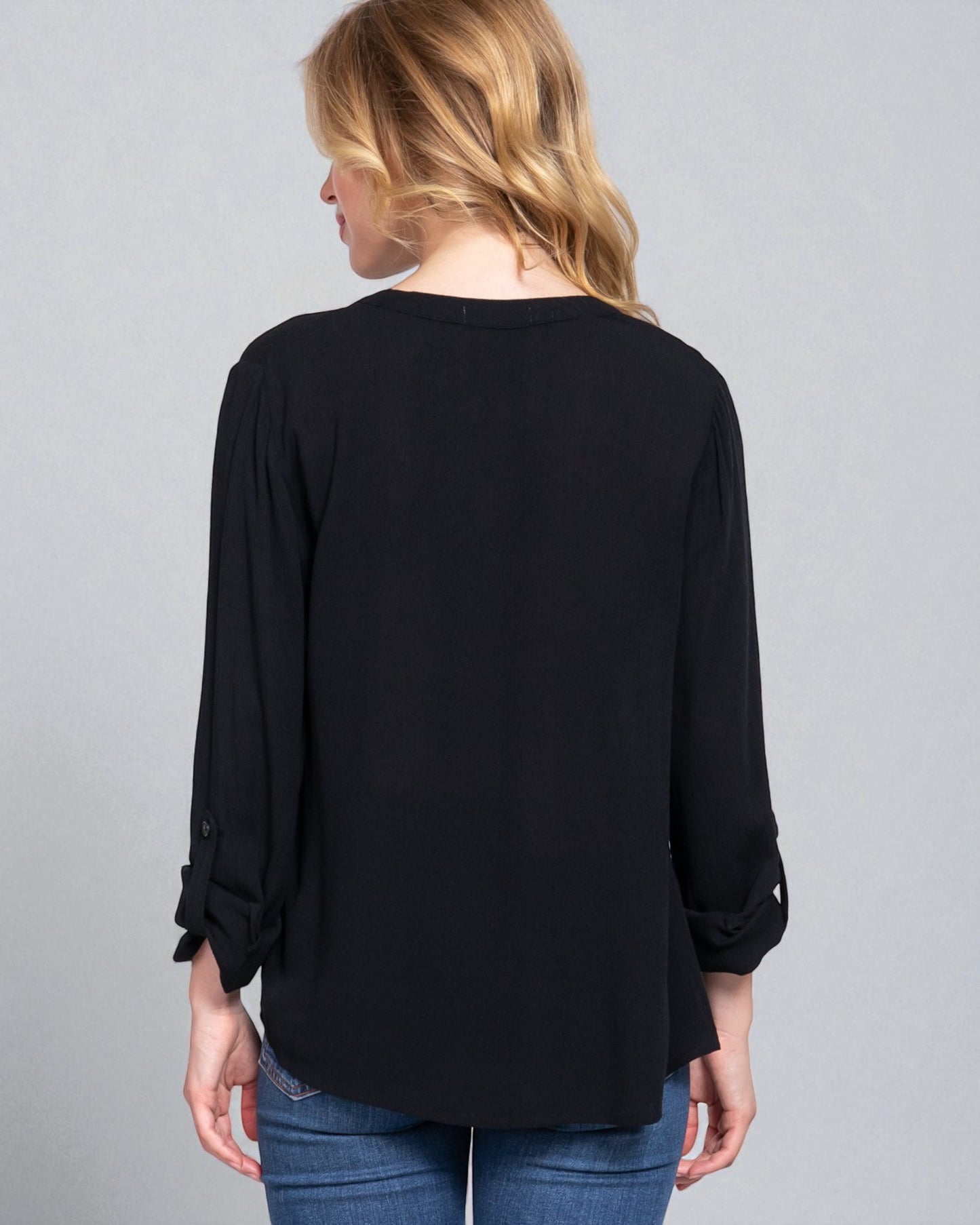 Person wearing a black long-sleeve top with rolled-up sleeves on a gray background