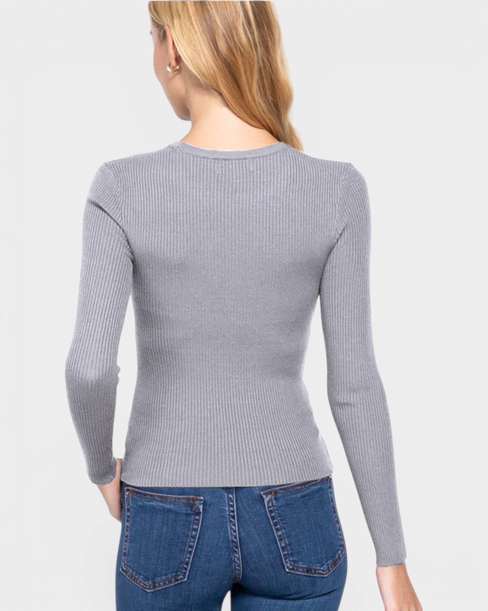 Woman wearing a gray ribbed sweater and blue jeans on a light gray background