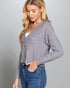Woman wearing a gray cardigan over a white top and blue jeans on a gray background