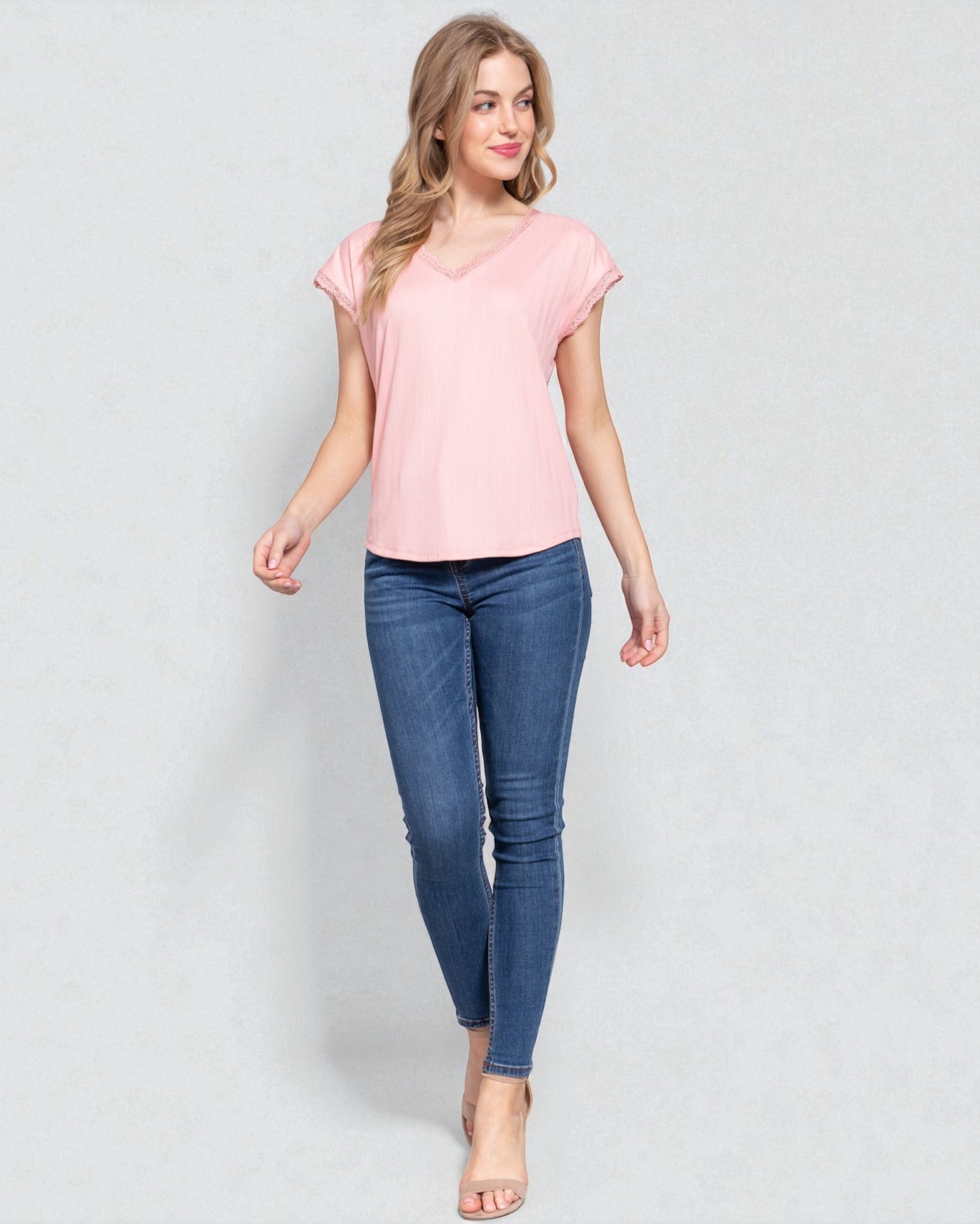 Woman wearing a pink top and blue jeans on a light gray background