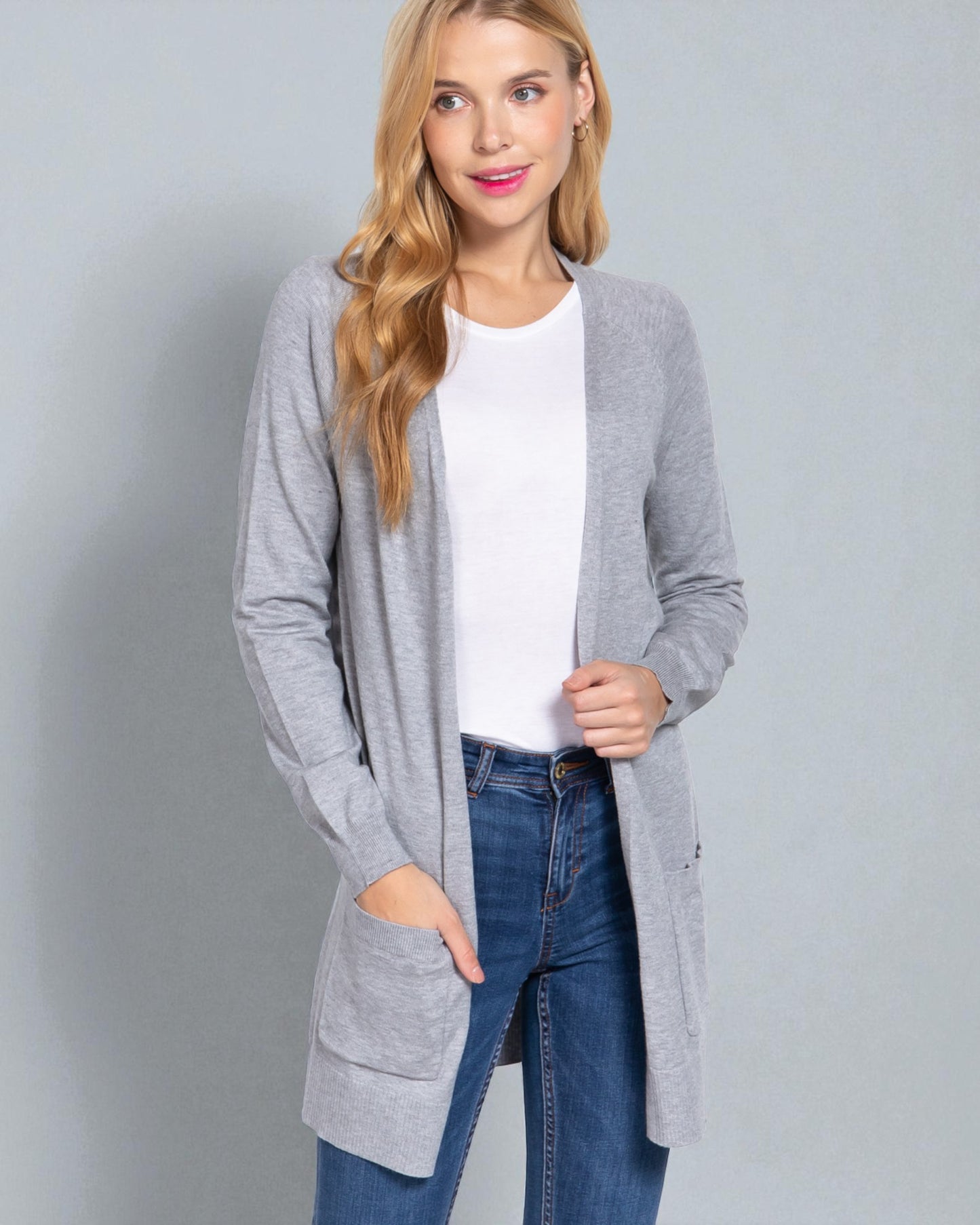 Woman wearing a gray cardigan over a white shirt and blue jeans on a gray background