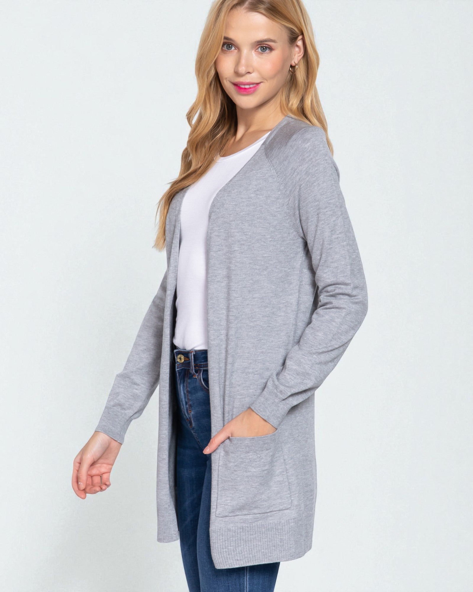 Woman wearing a gray cardigan over a white shirt and blue jeans on a light gray background