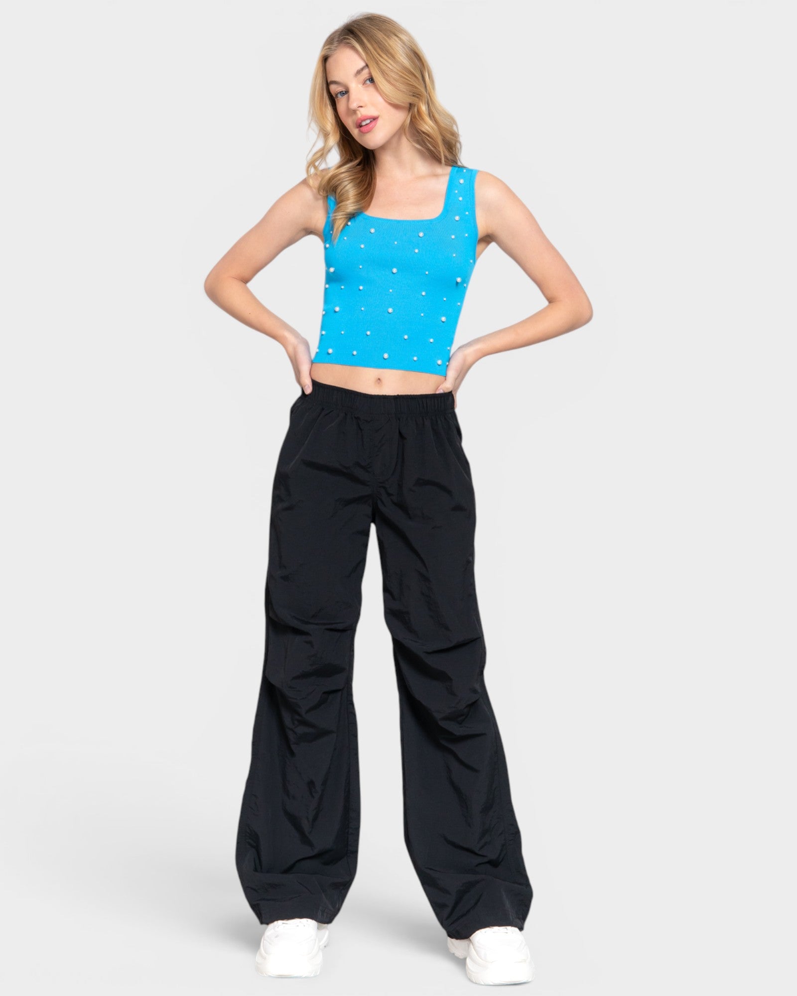 Woman wearing a blue tank top with white patterns and black pants on a white background