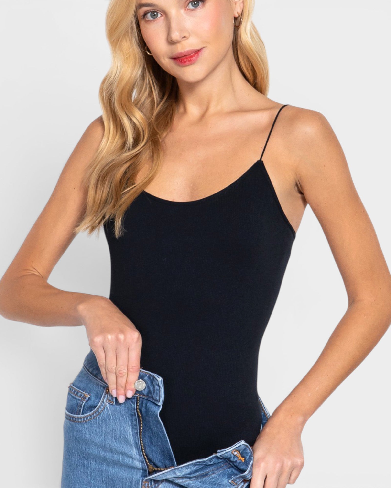 Woman wearing a black bodysuit and blue jeans against a white background