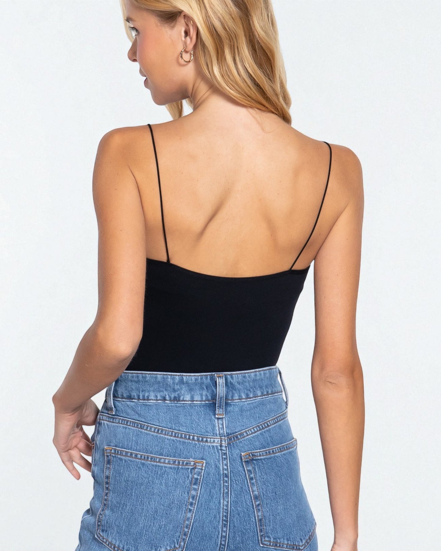 Woman wearing a black spaghetti strap top and blue jeans on a white background