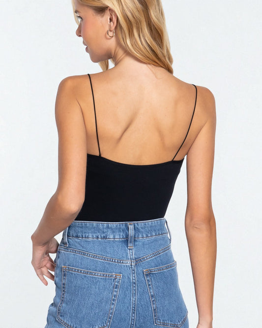 Woman wearing a black spaghetti strap top and blue jeans on a white background