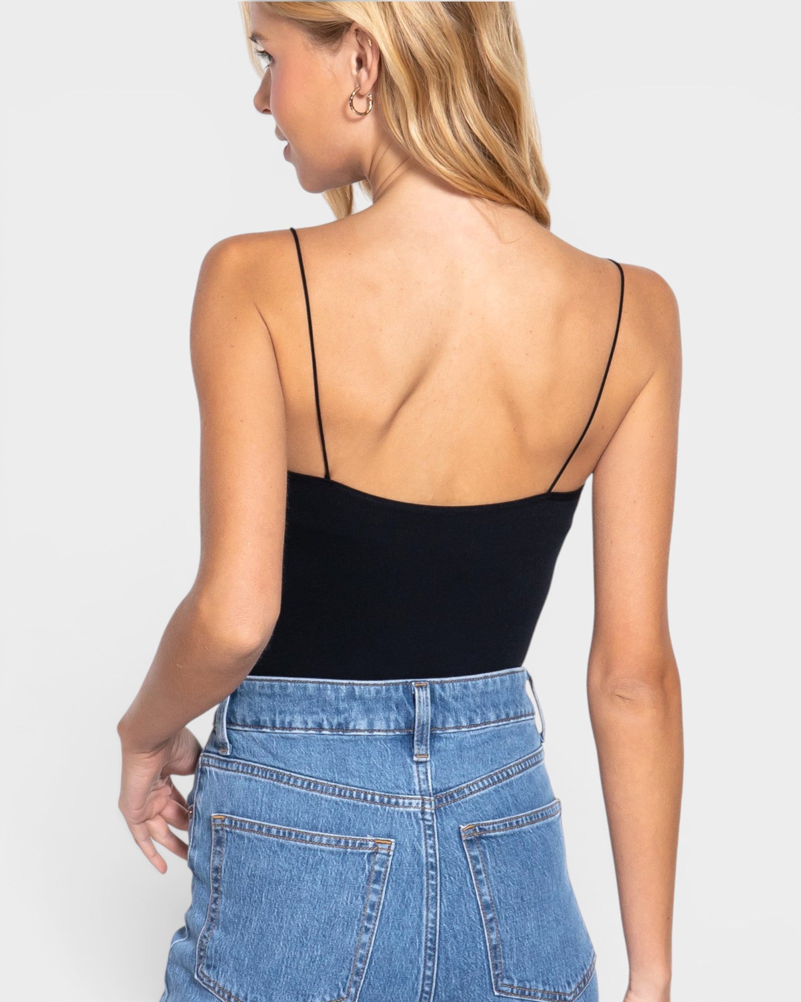 Woman wearing a black bodysuit and blue jeans against a white background