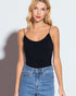 Woman wearing a black spaghetti strap top and blue jeans on a plain background