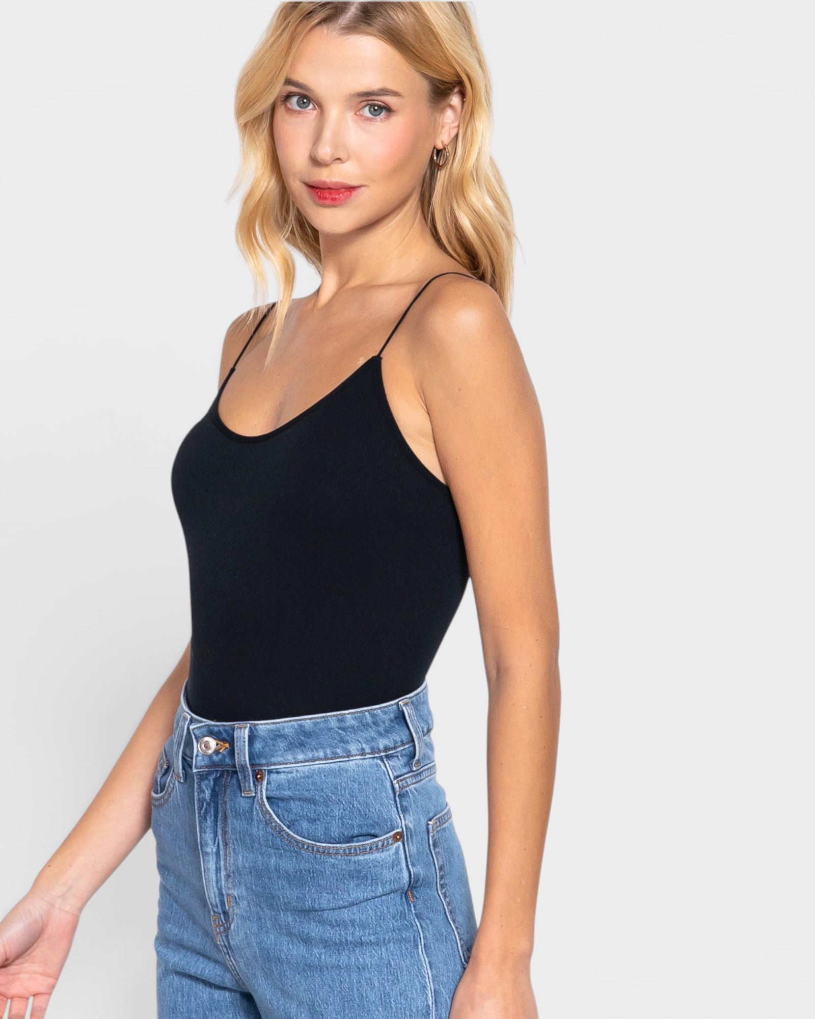 Woman wearing a black bodysuit and blue jeans against a white background
