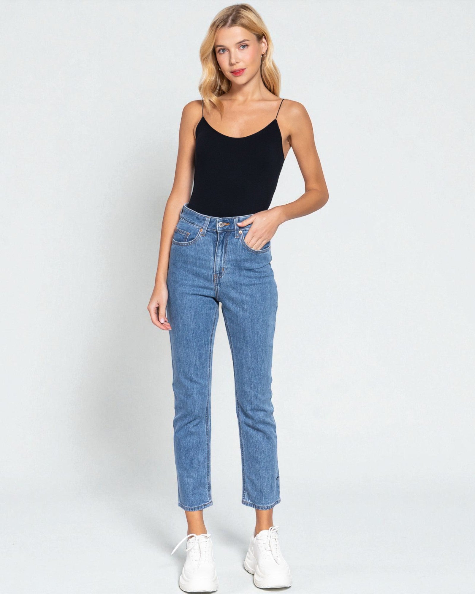 Woman wearing a black tank top and blue jeans on a white background