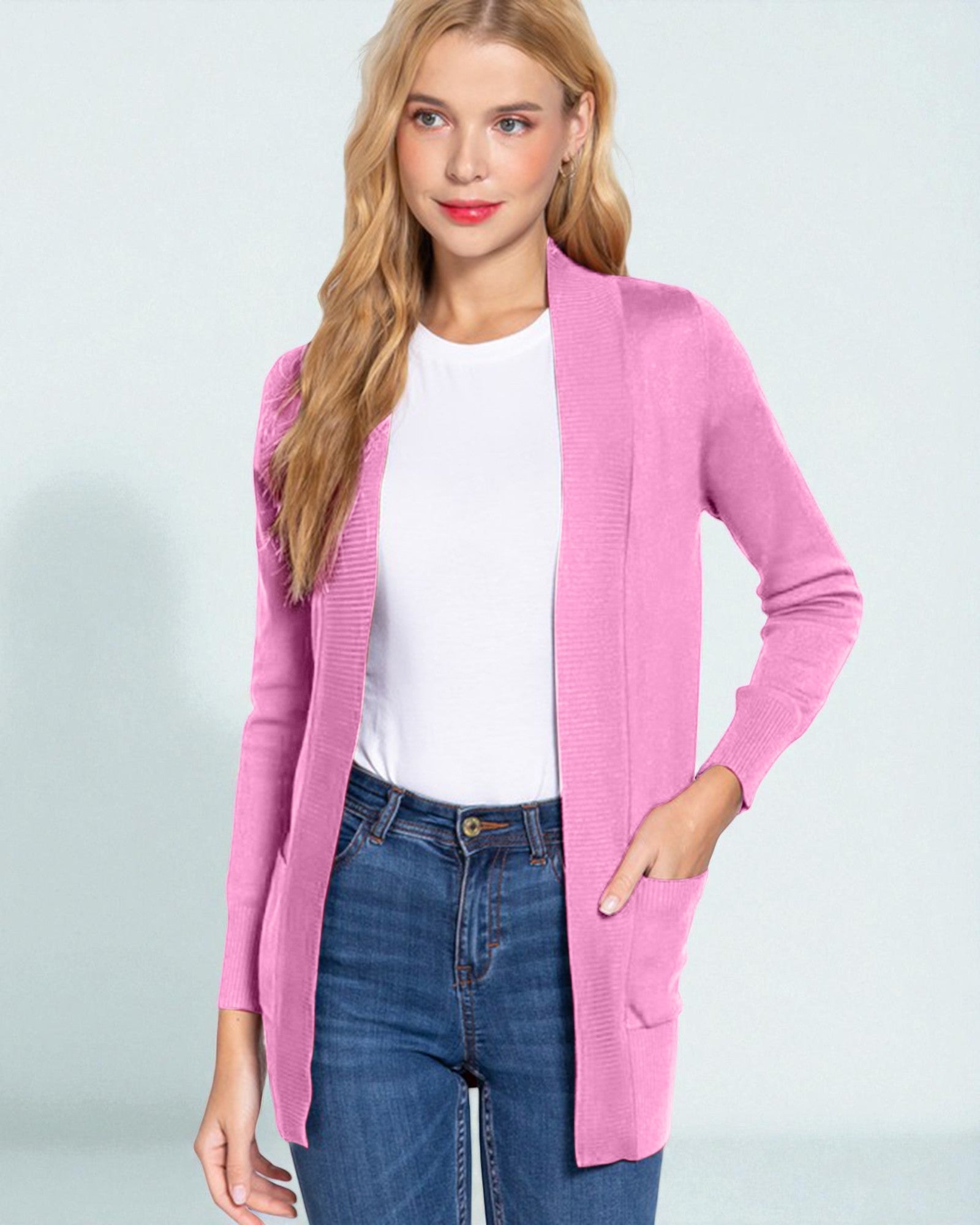 Woman wearing a pink cardigan over a white shirt and blue jeans on a light gray background