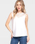 Woman wearing a white sleeveless top with lace details and blue jeans on a light gray background