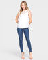 Woman wearing a white sleeveless top with lace details and blue jeans on a white background