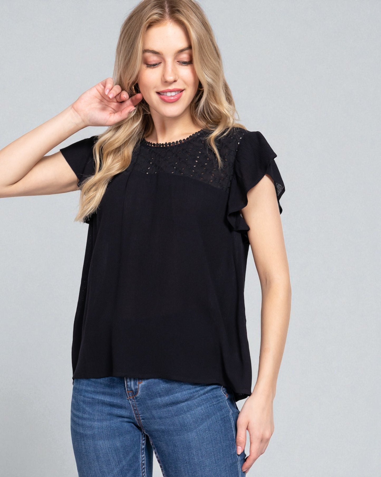 Woman wearing a black top with lace details and blue jeans on a gray background