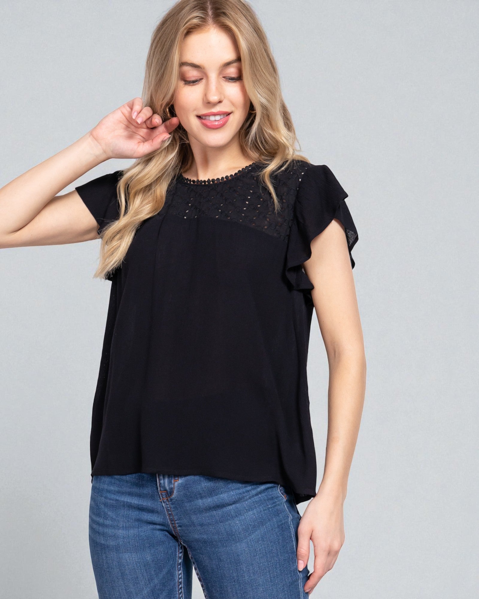 Woman wearing a black top with lace details and blue jeans on a gray background