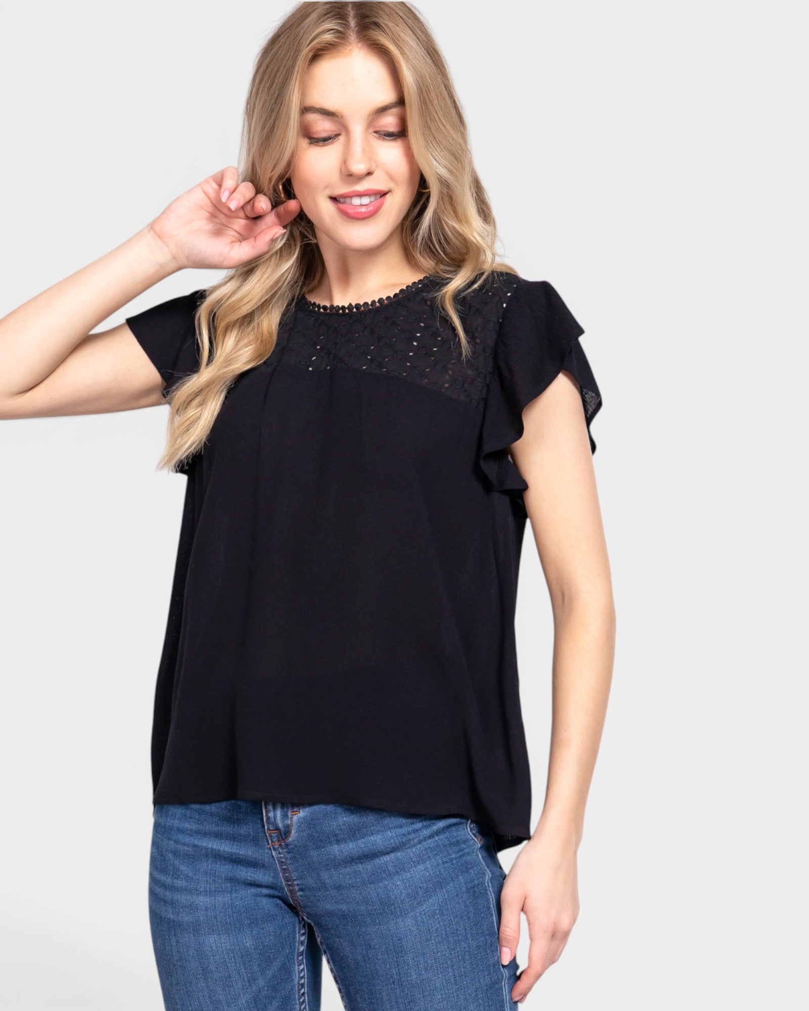 Woman wearing a black top with lace details and blue jeans on a white background