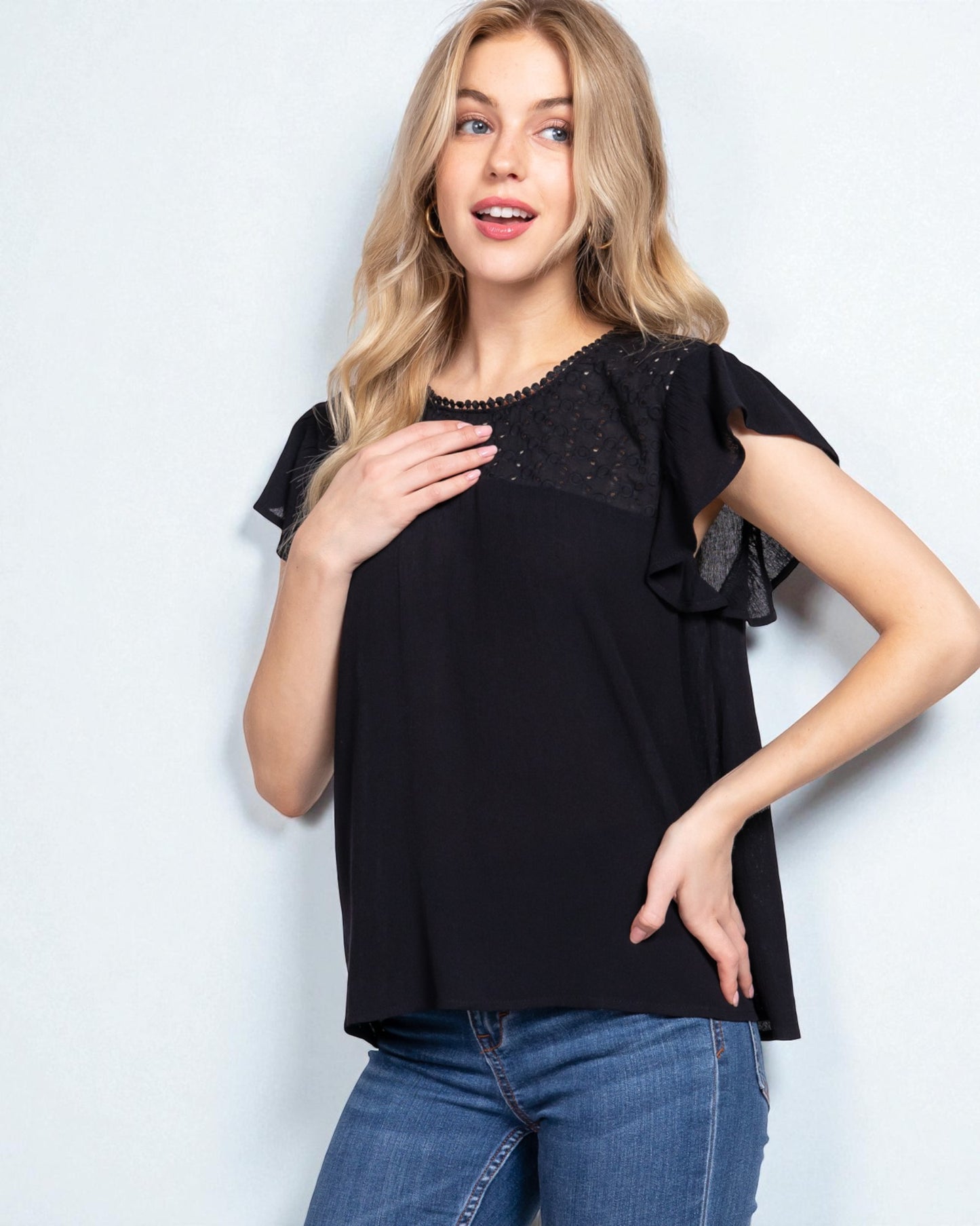 Woman wearing a black top with ruffled sleeves against a light background