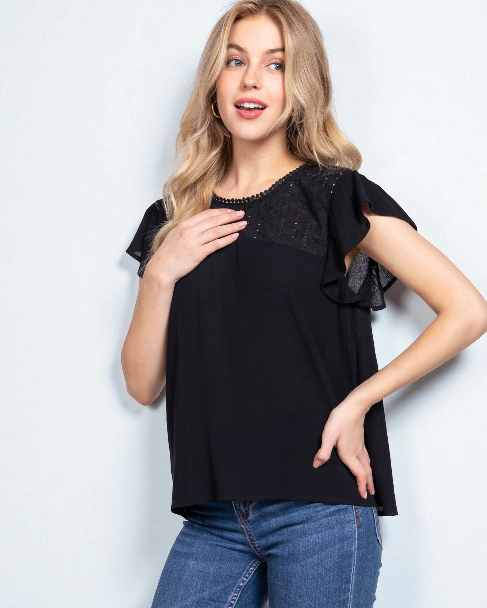 Woman wearing a black top with ruffled sleeves against a light background
