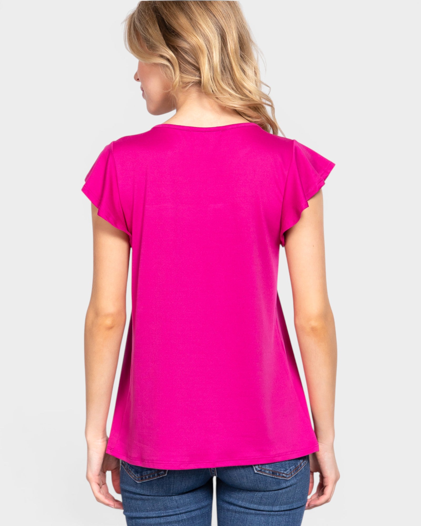 Woman wearing a bright pink top and blue jeans on a white background